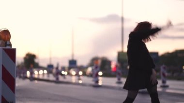 Aktif gezgin dansçı kadın siyah etek ve sıcak kazak ve bir chocker giyerek geçen araba ışıkları ile gün batımı nda bir yol şantiyede performans