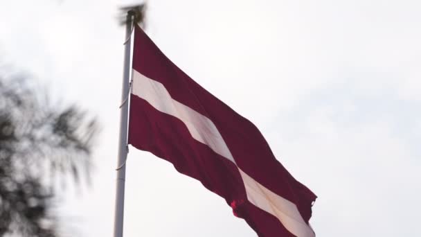 Latvisk flagg flagrer i vinden høyt oppe på himmelen under en gyllen solnedgang - Riga hovedstad i Latvia - Dambis AB - enormt nasjonalflagg – stockvideo