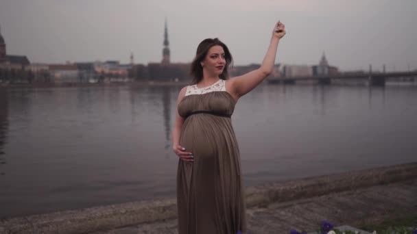 Mladá těhotná žena je šťastná ve své zemi cestovní destinace Lotyšsko s výhledem na město Riga a řeku Daugava - bílá běloška na sobě mateřské šaty — Stock video