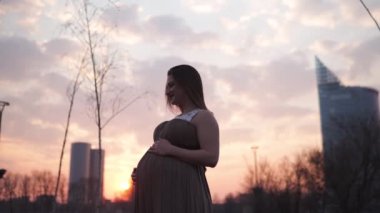 Göbek yakın holding - Genç hamile kadın şehir Riga ve nehir Daugava üzerinde bir görünüm ile onu seyahat hedef ülke Letonya mutlu - Beyaz beyaz kız hamile elbisesi giyiyor