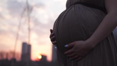 Göbek yakın holding - Genç hamile kadın şehir Riga ve nehir Daugava üzerinde bir görünüm ile onu seyahat hedef ülke Letonya mutlu - Beyaz beyaz kız hamile elbisesi giyiyor