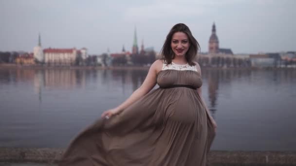 Счастливые танцы - молодая беременная женщина счастлива в стране назначения Латвия с видом на город Рига и реку Даугава - Белая кавказская девушка в материнском платье — стоковое видео