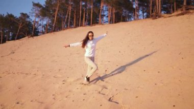 Genç bir kadın, Golden Hour 'da gün batımını yavaş çekimde seyrediyor. İlkbaharda, nehir kıyısında beyaz kum tepeciklerinde, beyaz pantolonları içinde, beyaz beyaz beyaz bir kız, mutlu bir koşu gezgini.