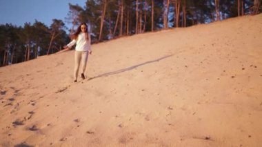 Genç bir kadın, Golden Hour 'da gün batımını yavaş çekimde seyrediyor. İlkbaharda, nehir kıyısında beyaz kum tepeciklerinde, beyaz pantolonları içinde, beyaz beyaz beyaz bir kız, mutlu bir koşu gezgini.