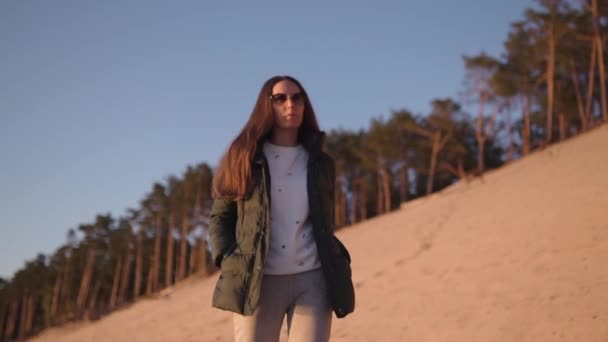 Young woman enjoys sunset during Golden Hour on a river beach in Spring wearing white pants, sweatshort and jacket - Caucasian white girl is a happy traveler — ストック動画