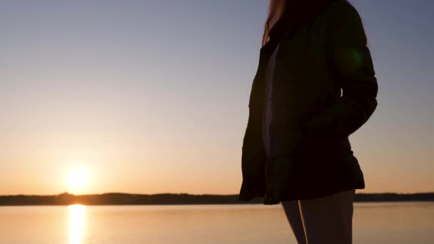 Giovane donna gode il tramonto durante Golden Hour su una spiaggia sul fiume in primavera indossando pantaloni bianchi, tuta corta e giacca - ragazza bianca caucasica è un viaggiatore felice — Video Stock