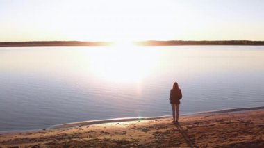 Genç bir kadın, baharda, bir nehir sahilinde gün batımını sever. Beyaz pantolon, kısa ceket ve beyaz ceket giyer. Beyaz, mutlu bir gezgin.