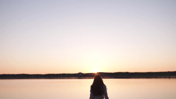 Giovane donna gode il tramonto durante Golden Hour su una spiaggia sul fiume in primavera indossando pantaloni bianchi, tuta corta e giacca - ragazza bianca caucasica è un viaggiatore felice — Video Stock