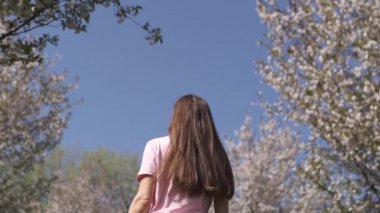 Yavaş Hareket 120fps: Genç mutlu gezgin kahverengi saçlı kadın kız gülümseyen ve Baltık eyaletlerinde pembe bir sakura kiraz çiçeği ağaçları ile yeni bir hedef ülkede etrafında dönüyor - Uçan saç