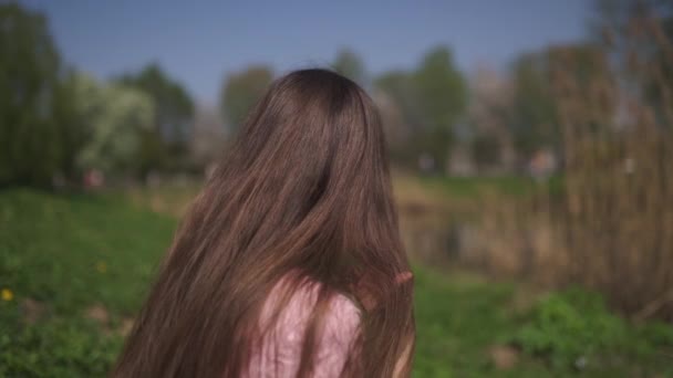 Zeitlupe 120fps: junge, glückliche Frau mit braunhaarigen Haaren lächelt und dreht sich um in einem neuen Zielland mit rosa Sakura-Kirschblütenbäumen in den baltischen Staaten - fliegendes Haar — Stockvideo