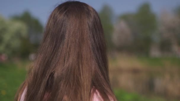 SLOW MOTION 120fps: Giovane viaggiatore felice donna dai capelli castani ragazza sorridente e girando in un nuovo paese di destinazione con un albero di ciliegio rosa sakura negli stati baltici - Capelli volanti — Video Stock