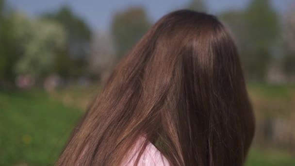 SLOW MOTION 120fps: Jovem feliz viajante de cabelos castanhos menina sorrindo e girando em um novo país de destino com um sakura rosa árvores flor de cerejeira nos estados bálticos - Cabelo voador — Vídeo de Stock