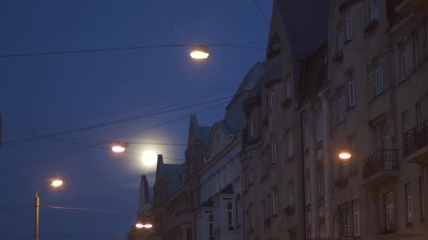 Ljus fullmåne synlig i stadens gator med tele foto objektiv med stadens ljus i förgrunden och Riga typiska builings i kvälls natten — Stockvideo