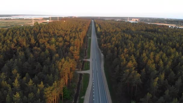 Lucht Sunrise shot van de weg buiten de stad in een landelijk bos met kaarten en vrachtwagens passeren kopen-Volg voertuig shot-top uitzicht van bovenaf — Stockvideo