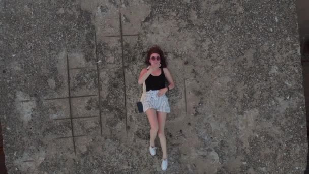 Aérea: Mujer turista viajero joven relajándose en una roca - sentimientos cálidos de verano - Chica blanca sexy caucásica caliente con pantalones cortos, camiseta negra y zapatillas blancas - Lindo encantador durante la puesta del sol — Vídeos de Stock