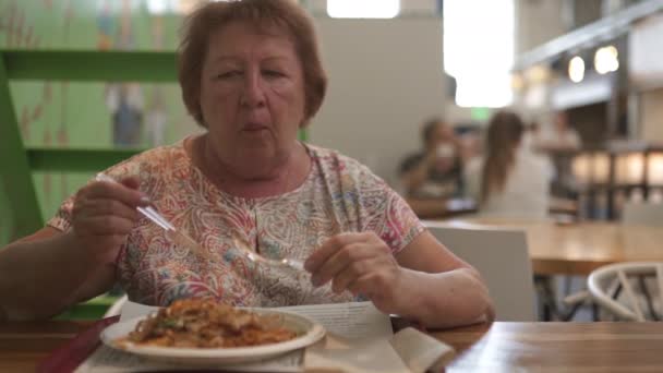 Ruiva mais velha sênior retiredf viagem turista mulher come no restaurante café vestindo luz rosa t-shirt com profundidade dop rasa de campo — Vídeo de Stock