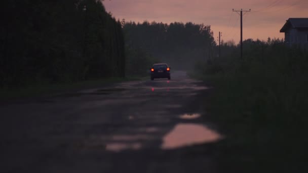 バックグラウンドで運転して通り過ぎる奇妙な車 - 赤とマゼンタ鮮やかな暗い色と雲と夕方に霧と不気味な場所 - ハロウィーンのテーマ - 怖い風景風景 — ストック動画