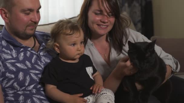 Сімейні цінності: мама і батько грають з дитиною хлопчик в приміщенні - величезна чорна пантера, як котяча кішка - Батьки в синьо-сірому домашньому одязі і їх син чорно-білий Щасливі усміхнені люди — стокове відео