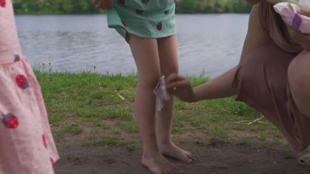 Joven madre hippie rubia teniendo tiempo de calidad con sus niñas limpiando las piernas sucias en un parque - Hijas usan vestidos similares con estampado de fresa - Valores familiares — Vídeos de Stock