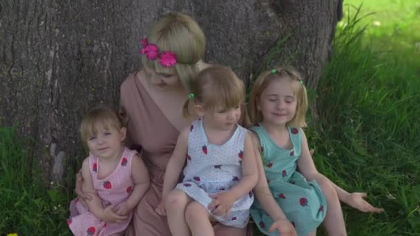 Jonge blonde hippie moeder met quality time met haar baby meisjes zitten en lachen onder een boom in een park - Dochters dragen soortgelijke jurken met aardbeienprint - Familie waarden — Stockvideo