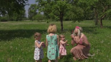 Genç sarışın hippi anne parkta sabun köpüğü üfleyerek güzel vakit geçiriyor kızlar da çilek desenli benzer elbiseler giyiyor aile değerleri kavramı.