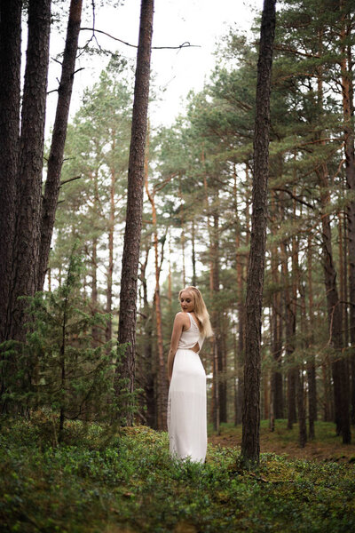 Beautiful young blonde woman forest nymph in white dress in evergreen wood - European caucasian with freckles