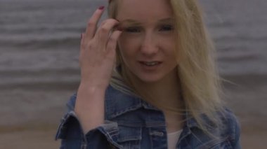 Fırtınalı rüzgar ve yağmur ile donuk kasvetli havalarda dalgalar ile deniz kenarında beyaz elbise güzel genç sarışın kadın plaj perisi portresi - Mavi kot ceket