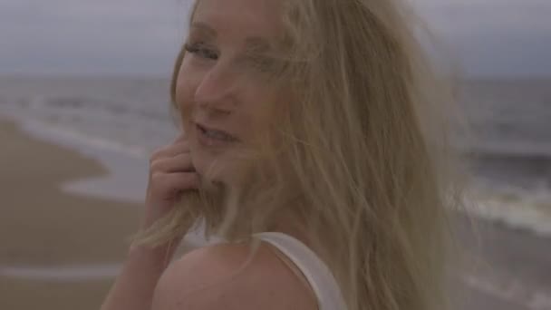 Primer plano retrato de hermosa joven rubia playa ninfa en vestido blanco cerca del mar con olas durante un clima sombrío aburrido con viento tormentoso y lluvia — Vídeos de Stock