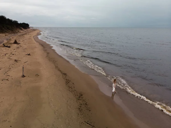 Légi gyönyörű fiatal szőke nő strand nimfa fehér ruhában a tenger közelében a hullámok alatt unalmas komor Időjárás viharos szél és az eső — Stock Fotó