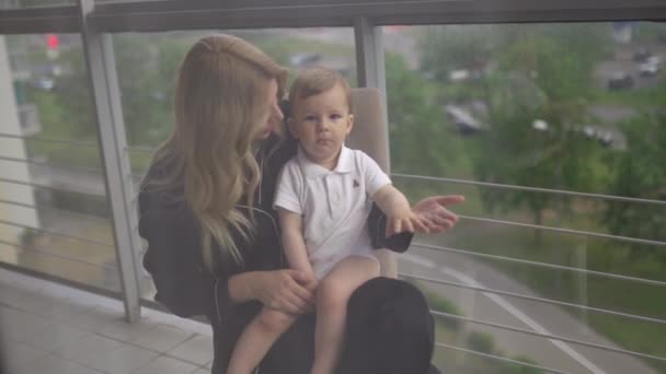 Spielen auf dem Balkon - junge blonde Mutter hat Zeit mit ihrem kleinen Sohn in der Wohnung der Familie - trägt schwarzes Budoir-Kleid Kostüm Schlafmantel — Stockvideo