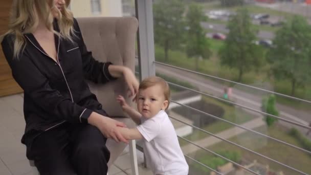 Spela på balkongen-ung blondin mamma har kvalitetstid med sin baby pojke son på familjens hem platt-klädd svart budoir klänning kostym sovande klänning — Stockvideo
