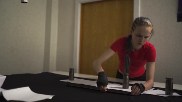 Diseñadora de moda cyber punk en el trabajo en su patrón de corte de estudio - Mujer blanca caucásica con camiseta roja y guantes negros con tijeras colgando sobre su pecho — Vídeos de Stock