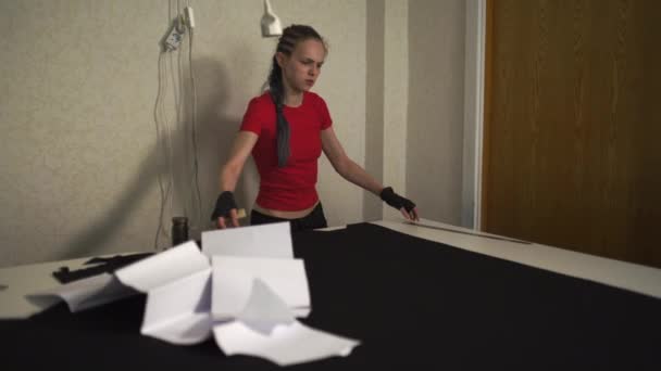 Diseñadora de moda cyber punk en el trabajo en su patrón de corte de estudio - Mujer blanca caucásica con camiseta roja y guantes negros con tijeras colgando sobre su pecho — Vídeos de Stock