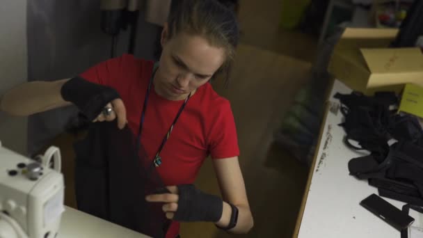 Diseñadora de moda cyber punk en el trabajo en su estudio de costura con máquina - Mujer blanca caucásica con camiseta roja y guantes negros con tijeras colgando sobre su pecho — Vídeos de Stock