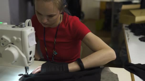 Diseñadora de moda cyber punk en el trabajo en su estudio de costura con máquina - Mujer blanca caucásica con camiseta roja y guantes negros con tijeras colgando sobre su pecho — Vídeo de stock