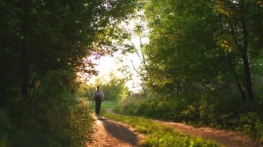 Pantolon ve beyaz gömlek yürüyüş Redhead kadın - Güzel akşam güneş ışığı ışınları ile yol sunset ülke, çevresinde yeşil yaprak ağaçları - Doğa arka planda dinlenmek için harika bir yerdir