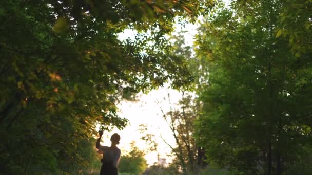 바지와 흰색 셔츠 포즈에 빨간 머리 여자 - 아름다운 저녁 태양 광선, 주변의 녹색 잎 나무와 도로 오프 일몰 국가 - 자연은 배경에서 휴식을 취할 수있는 좋은 장소입니다 — 비디오