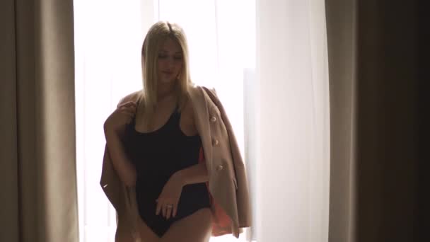 Ung vacker mode kvinna porträtt tittar på kameran - kaukasiska blond flicka hemma waring biege jacka och svart kropp - Smidig cinematic handhållen rörelse — Stockvideo