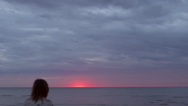 Junge Frau in weißem Kleid sitzt im Vordergrund auf einer Decke und genießt den seltenen glühenden Himmel der Natur - erstaunlich dunkel szenisch lebhaft purpurrot seltener Sonnenuntergang — Stockvideo