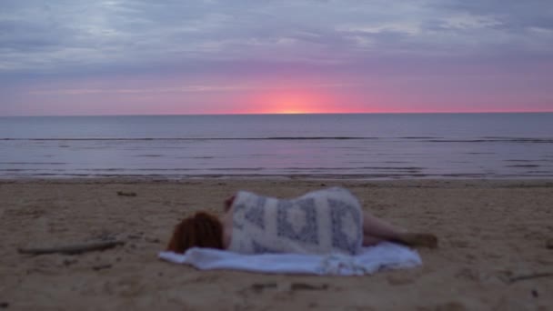 Fiatal nő lány fehér ruhában feküdt az előtérben egy takarón, és élvezi a ritka izzó természet ég - Csodálatos sötét festői élénk bíbor ritka vörös naplemente — Stock videók
