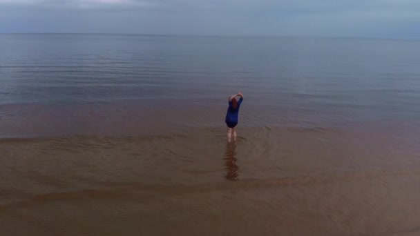 Aérienne : Jeune femme en robe bleue lumineuse se promenant - Paysage pittoresque de coucher de soleil jaunâtre en eau peu profonde à la mer Baltique - Drone volant vue d'en haut — Video