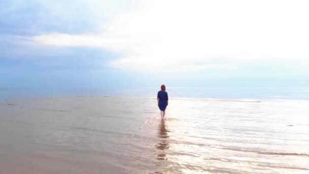空中:青い明るいドレスを着た若い女性が歩き回る - バルト海の浅瀬風光明媚な黄色がかった夕日の風景 - 上空からドローン飛行 — ストック動画