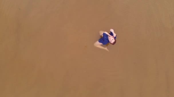 Aerea: Giovane donna in abito blu brillante sdraiata - acqua bassa scenico paesaggio giallastro tramonto sul Mar Baltico - Drone vista volante dall'alto — Video Stock