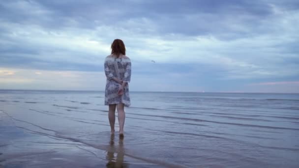 Menina jovem em um vestido branco de pé e andando em primeiro plano e desfrutando do céu da natureza - incrível escuro cênico vívido carmesim raro pôr do sol vermelho — Vídeo de Stock