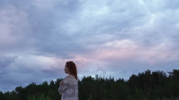 Menina jovem em um vestido branco em primeiro plano e desfrutando de raro brilho céu natureza Moody pôr do sol frio com cores azuladas magenta vívidas no Golfo do Mar Báltico no verão — Vídeo de Stock