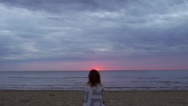 Junge Frau in weißem Kleid sitzt im Vordergrund auf einer Decke und genießt den seltenen glühenden Himmel der Natur - erstaunlich dunkel szenisch lebhaft purpurrot seltener Sonnenuntergang — Stockvideo