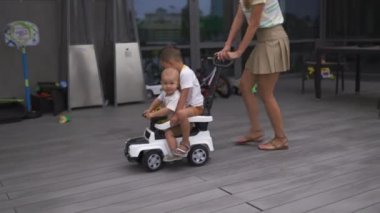 Genç anne oynarken ve araba ile yeşil bir bahçede onun bebek erkek erkek kardeşi ile eğlenmek - Aile değerleri sıcak renk yaz sahnesi