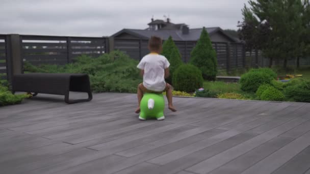 Niño bebé hijo saltando caballo de juguete verde en un jardín verde - Valores de la familia escena de verano de color cálido — Vídeos de Stock