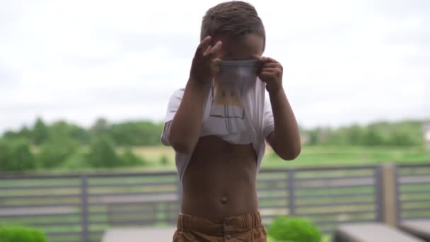 Close-up gezicht portret: schattige jongen op zoek en glimlachend op camera staande-ondiepe diepte van het veld-opheffing van zijn t-shirt — Stockvideo