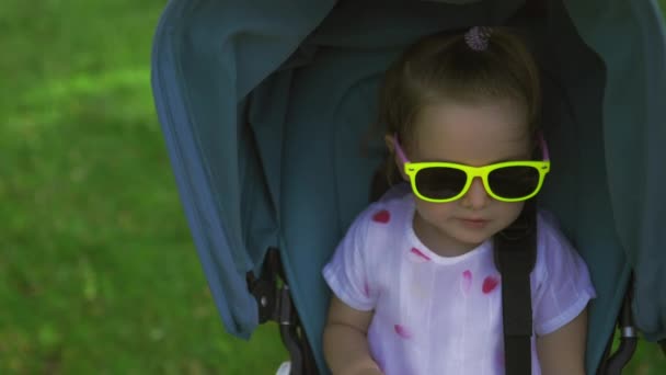 Close-up: schattig meisje op zoek en glimlachend op camera zittend in blauwe baby vervoer-familie waarden warme kleur zomer scène-blanke blanke — Stockvideo